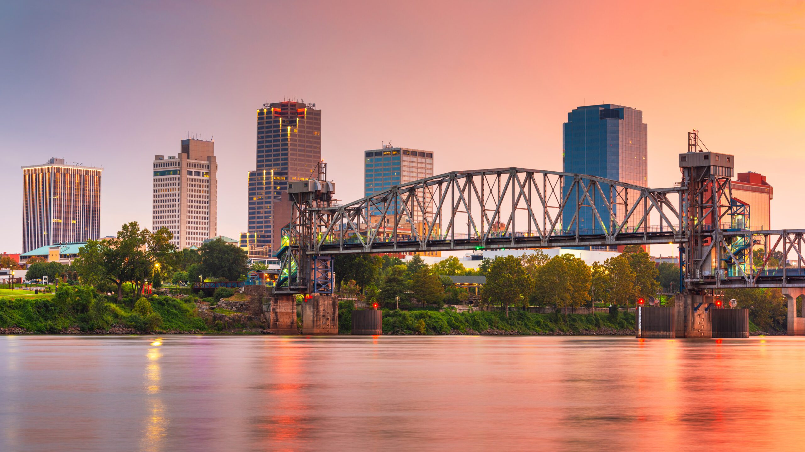 Scenic view of the Little Rock, Arkansas skyline at sunset with the river and bridge in the foreground.